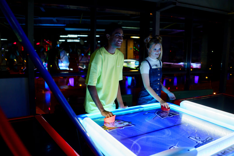 People playing air hockey in a neon-lit arcade